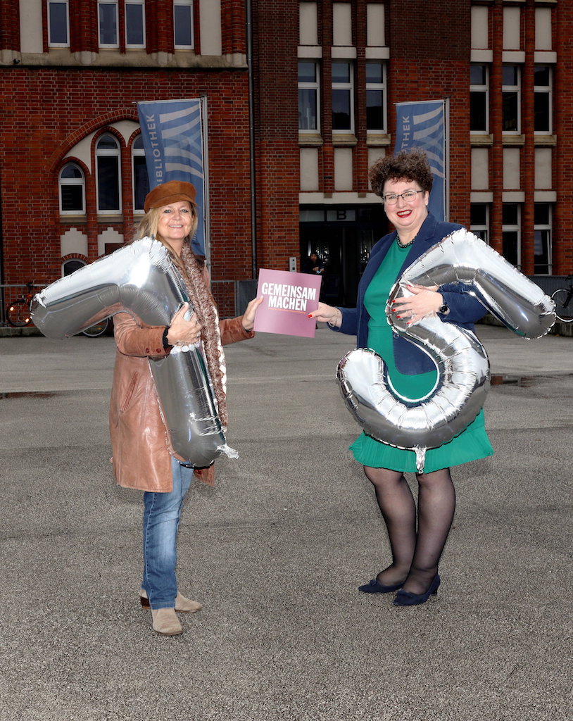  – Fröhlich präsentieren Marina Friedt, Vorsitzende des DJV Hamburg (l.) und Dr. Sabine Bamberger-Stemmann, Direktorin der Hamburger Landeszentrale für Politische Bildung, das Jubiläumsbuch vor der Zentralbibliothek. Foto: Florian Büh